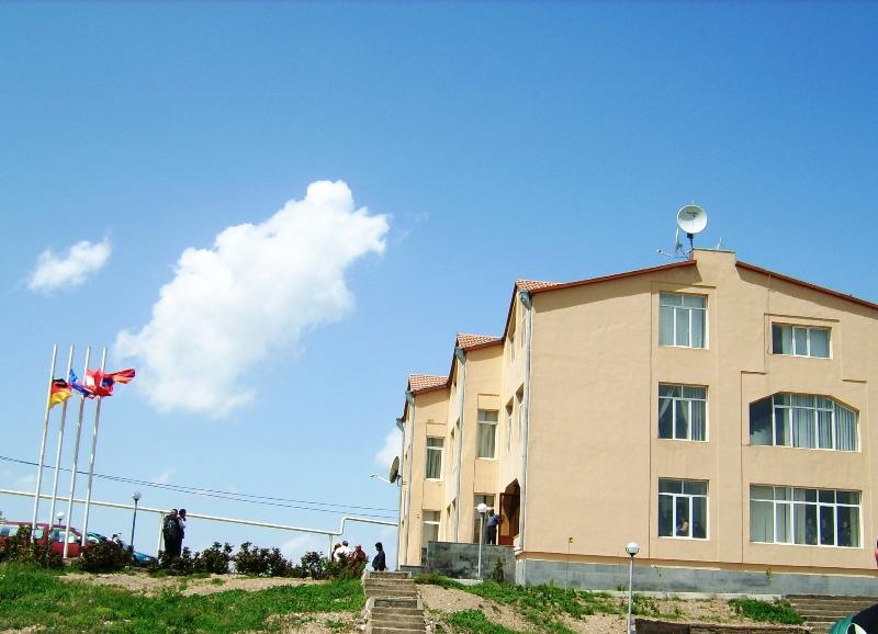 Das Verwaltungsgebäude im Dorf der Hoffnung - Ein dreistöckiges helles Gebäude mit Satteldach, daneben vier Fahnenstangen mit Fahnen