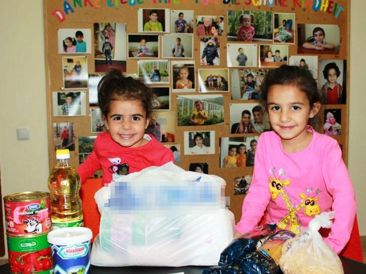 Zwei Mädchen stehen vor einer Fotowand, vor sich einige Lebensmittel und eine volle Tüte