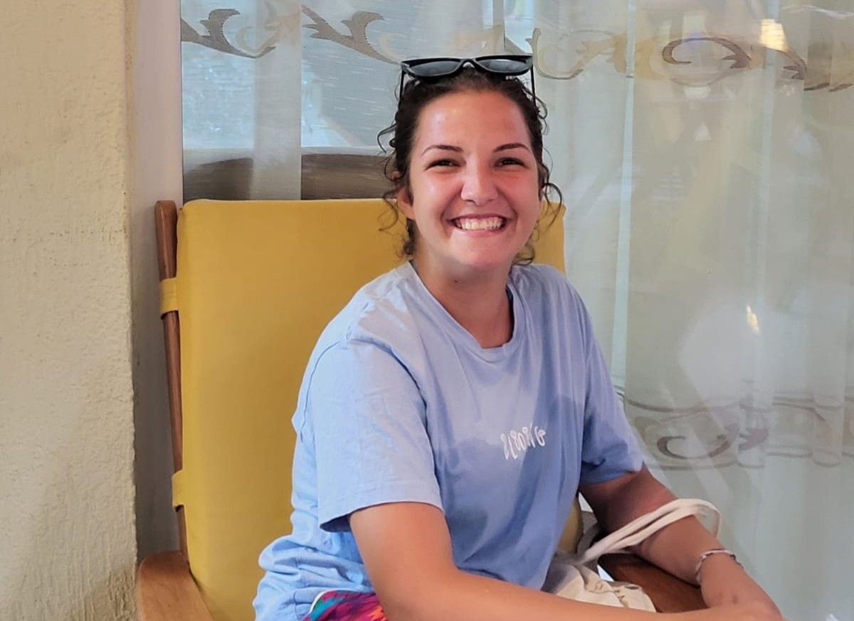 Eine junge Frau sitzt auf einem Stuhl und lächelt breit in die Kamera.