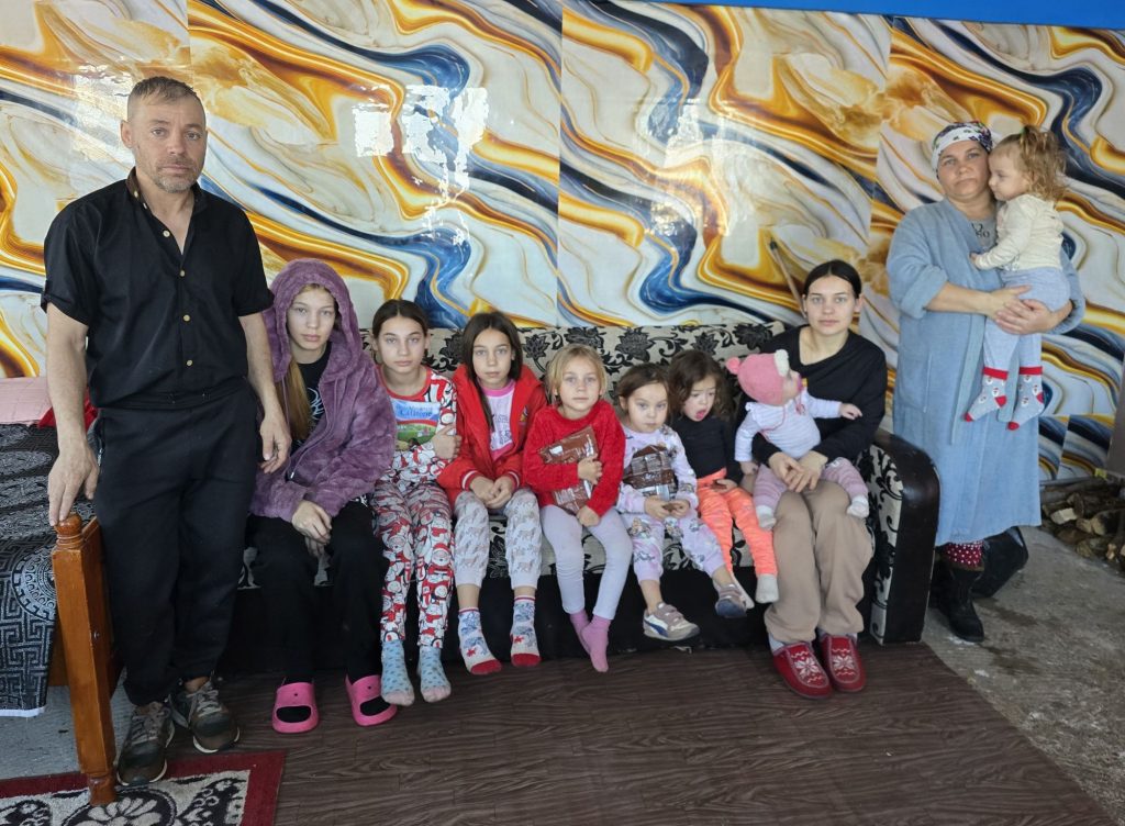 Acht Kinder und Jugendliche sitzen auf einem Sofa, links daneben steht der Vater, rechts daneben die Mutter mit einem Kind auf dem Arm