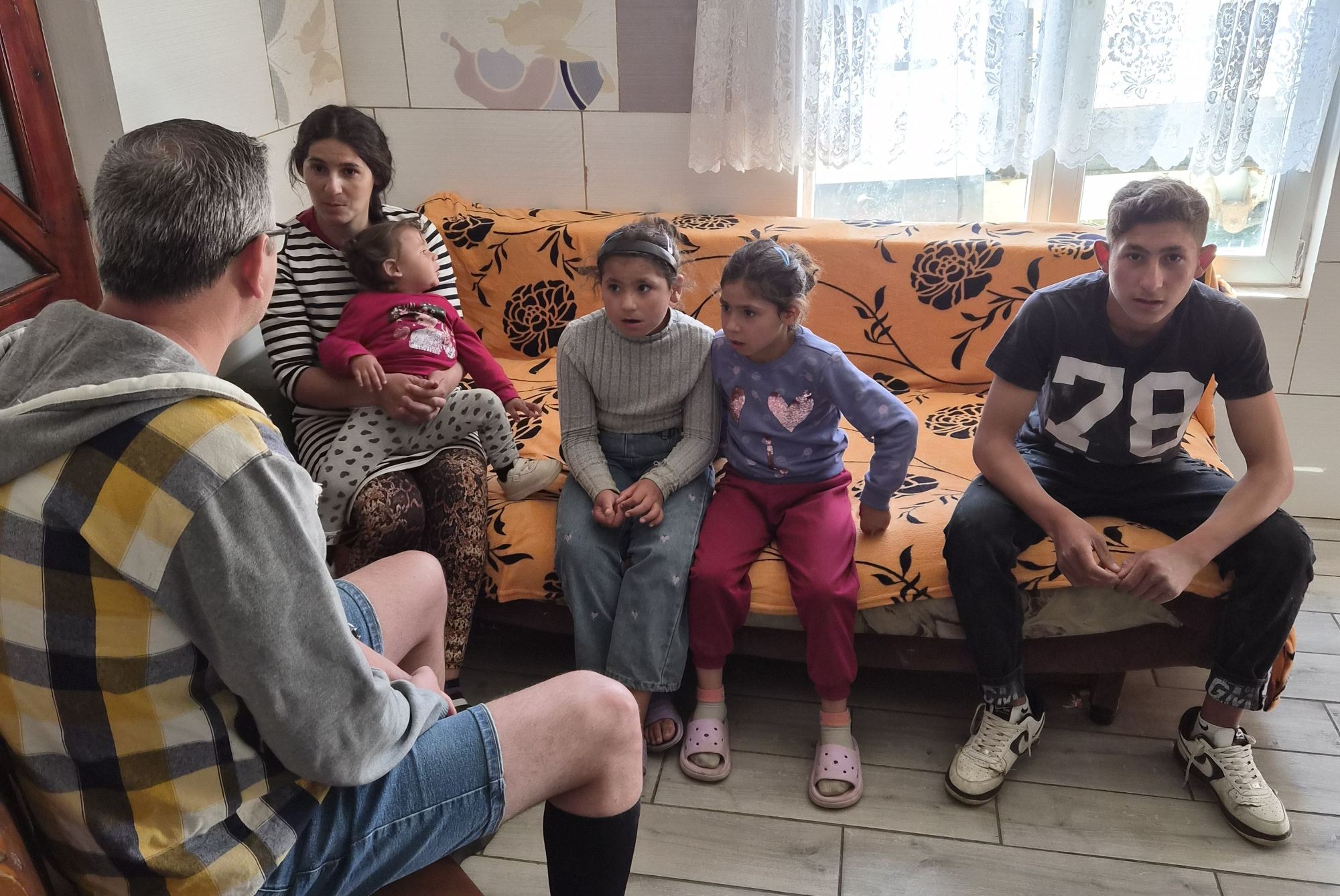 Eine Frau und vier Kinder sitzen auf einem Sofa; ihnen gegenüber sitzt der Mitarbeiter einer Hilfsorganisation
