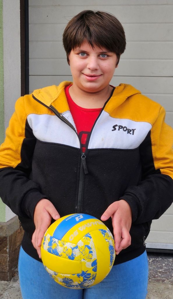 Ein Mädchen lächelt in die Kamera; sie hält einen Ball in den Händen