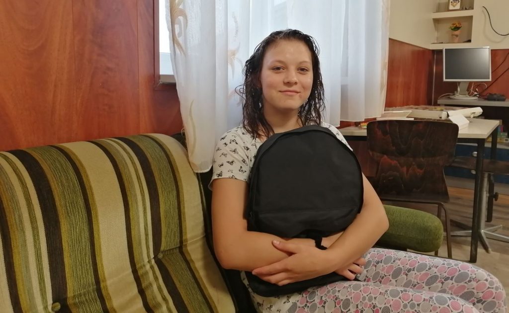 Ein junges Mädchen sitzt auf einem Sofa und hält einen Rucksack im Arm