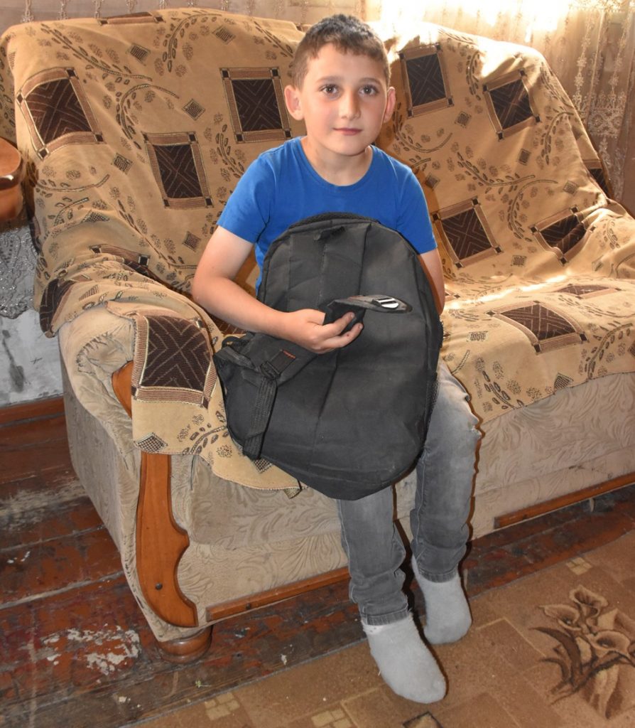 Ein Junge sitzt auf einem Sofa und zeigt seinen kaputten Schulrucksack.