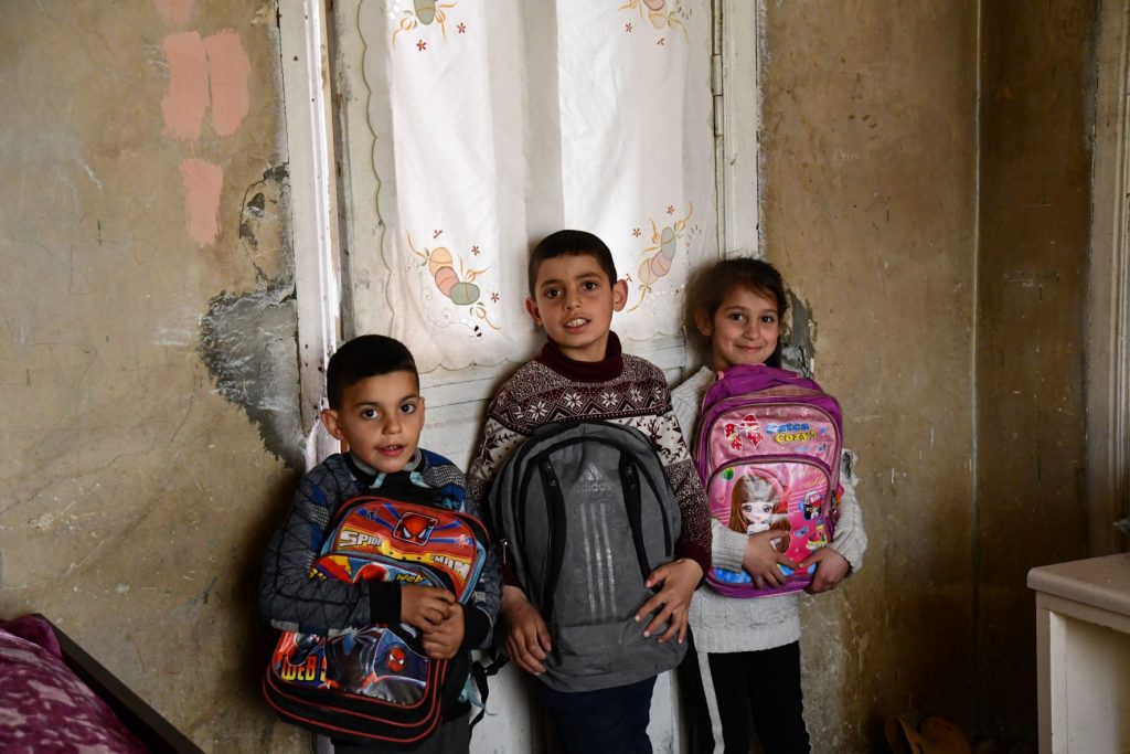 Zwei Jungen und ein Mädchen stehen nebeneinander und halten ihre Schulrucksäcke in den Händen
