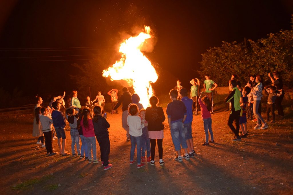 Sommercamp - Kinder stehen im Dunkeln um ein hohes Feuer
