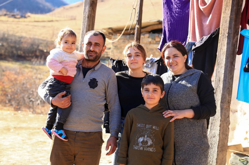 Ein Mann mit einem kleinen Mädchen auf dem Arm, eine Frau, ein Teenager-Mädchen und ein Junge stehen im Freien vor aufgehängten Decken.
