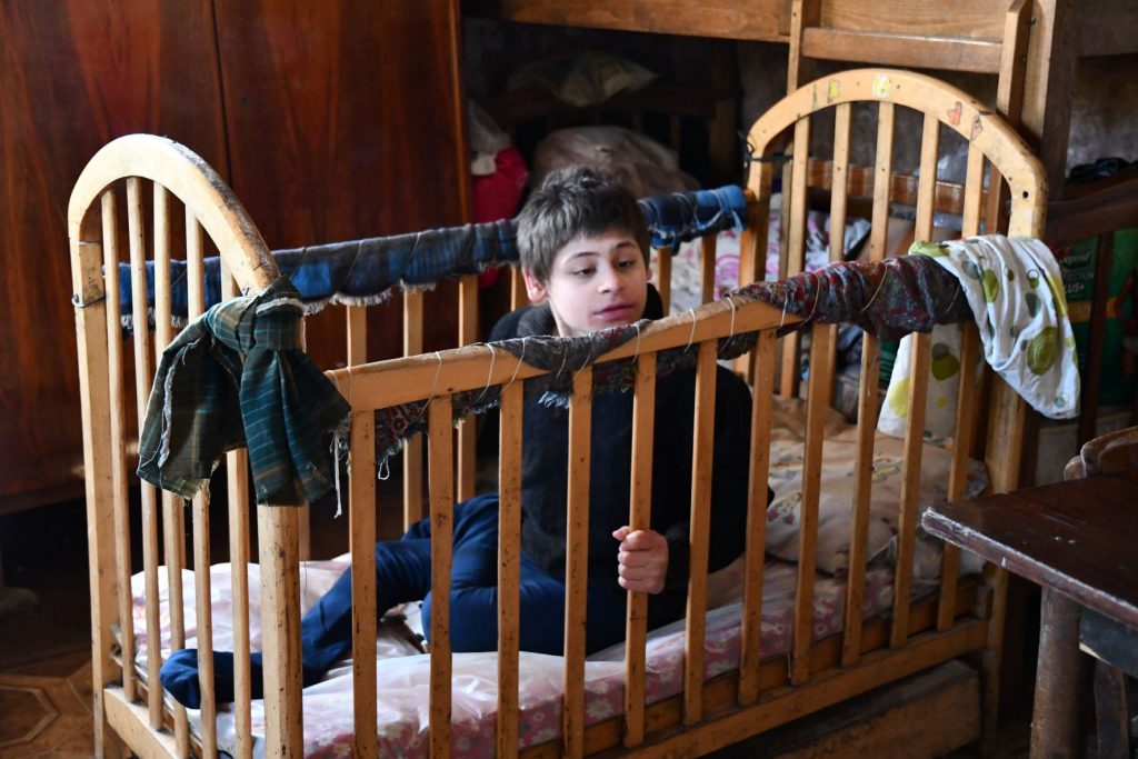 A disabled teenage boy sits in a cot with high bars