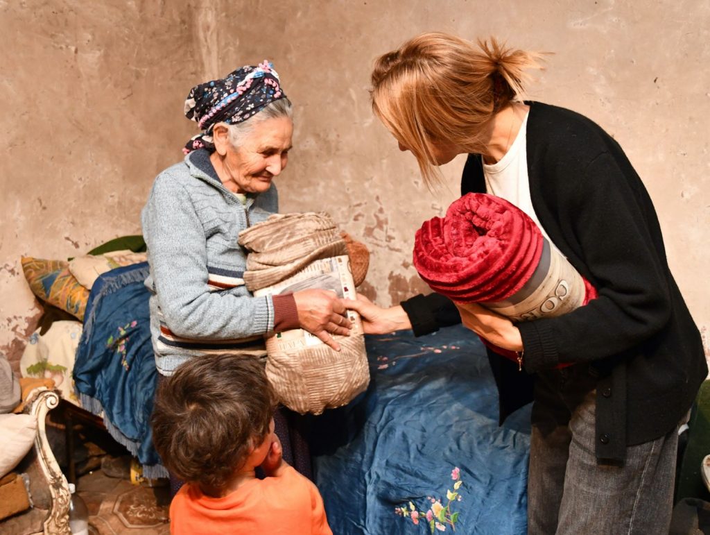 An elderly woman receives a warm blanket from a younger woman