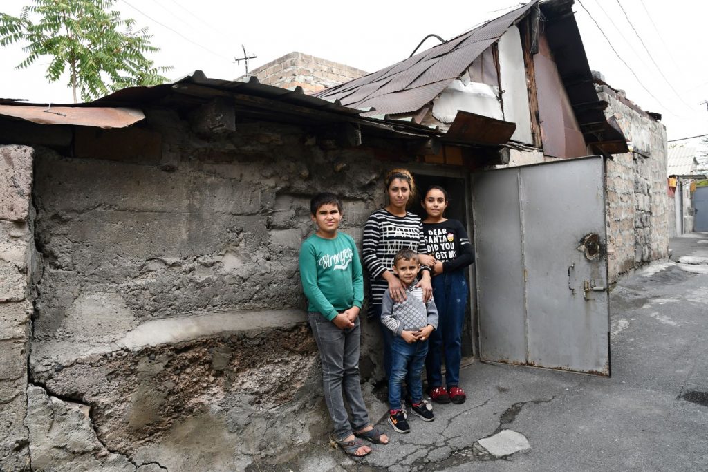 A woman and her three children are standing in front of a run-down house.