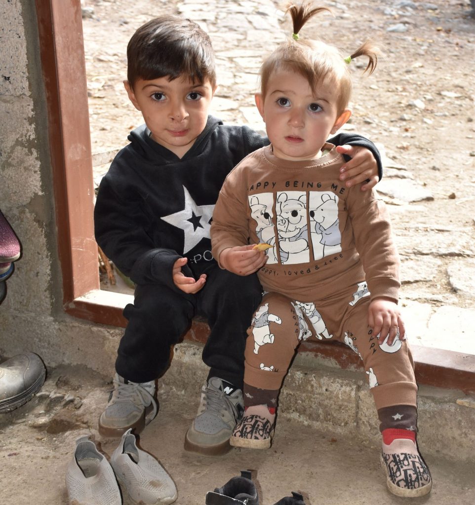 Ein kleiner Junge und ein kleines Mädchen sitzen in einem Türrahmen. Der Junge hat den Arm um das Mädchen gelegt.