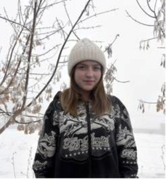 Älteres dunkelblondes Mädchen mit heller Pudelmütze und dunkler Winterjacke mit weißem Muster steht im Schnee